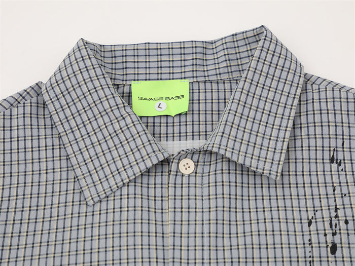 Close-up of shirt collar and top button on gray plaid fabric with black paint splatter