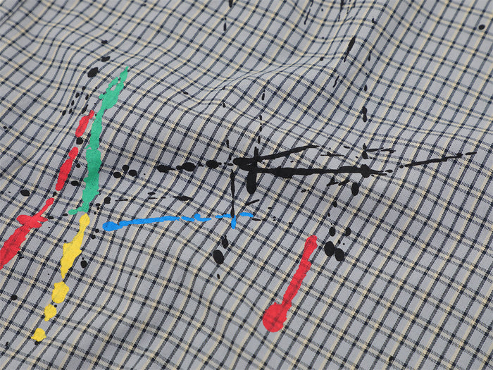 Close-up of gray plaid shirt fabric with multicolor paint splatter and chest seam detail