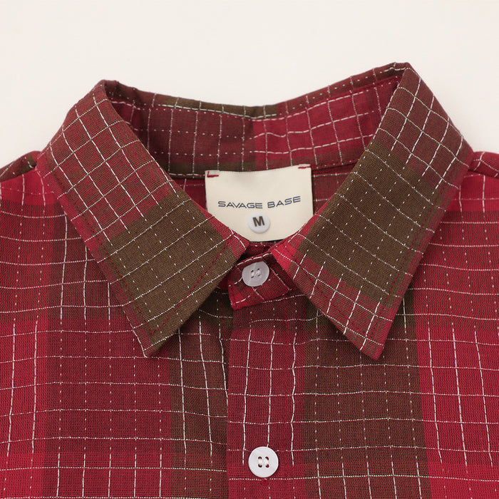 Red and brown plaid button-up shirt with oversized collar and white buttons on a light background
