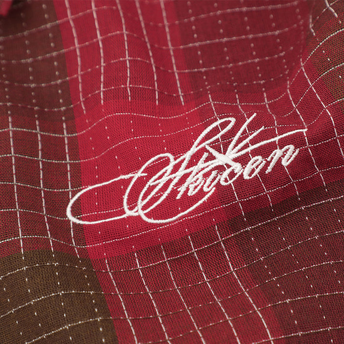Close-up of red mosaic plaid fabric with white script embroidery on an oversized short sleeve button-up shirt