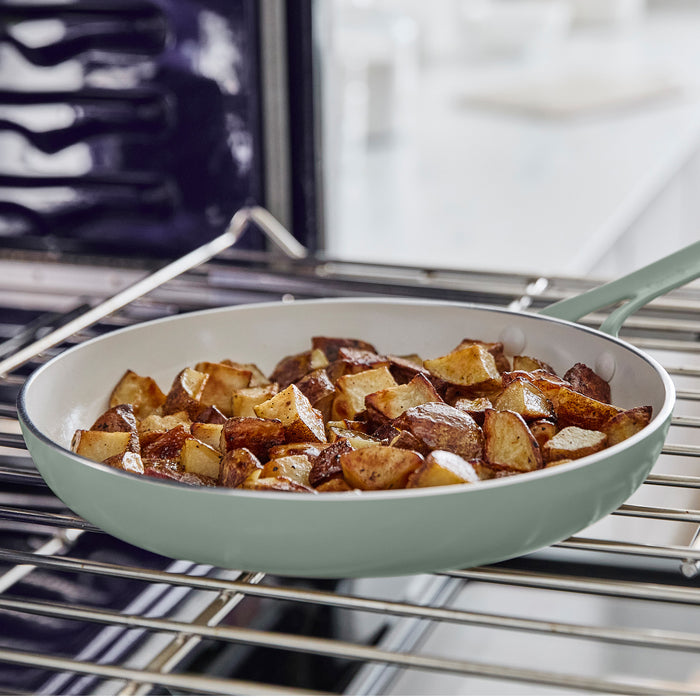 Green frying pan with roasted potatoes on a metal oven rack