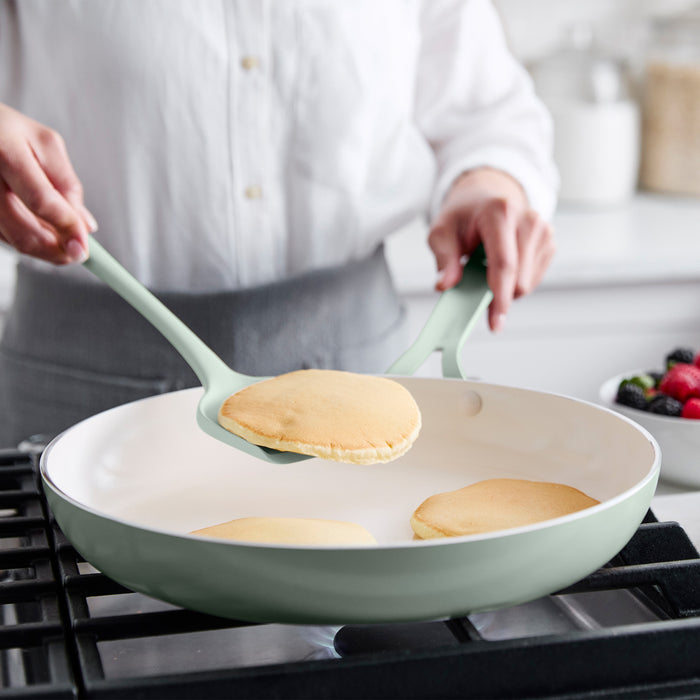 Person cooking pancakes in a green pan with a turner