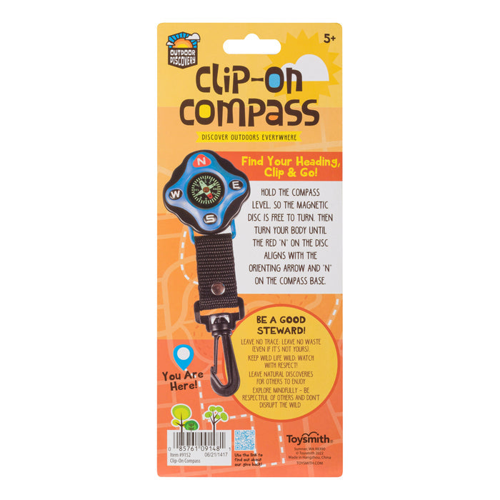 The image shows the packaging of an Outdoor Discovery Clip On Compass for ages 5+, featuring kids navigation tips, a colorful compass illustration, and a brown strap with an orange clip—ideal for outdoor adventures.