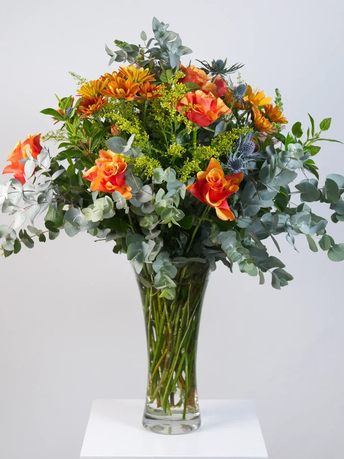 Large orange rose, gerbera and blue thistle bouquet with eucalyptus in trumpet glass vase