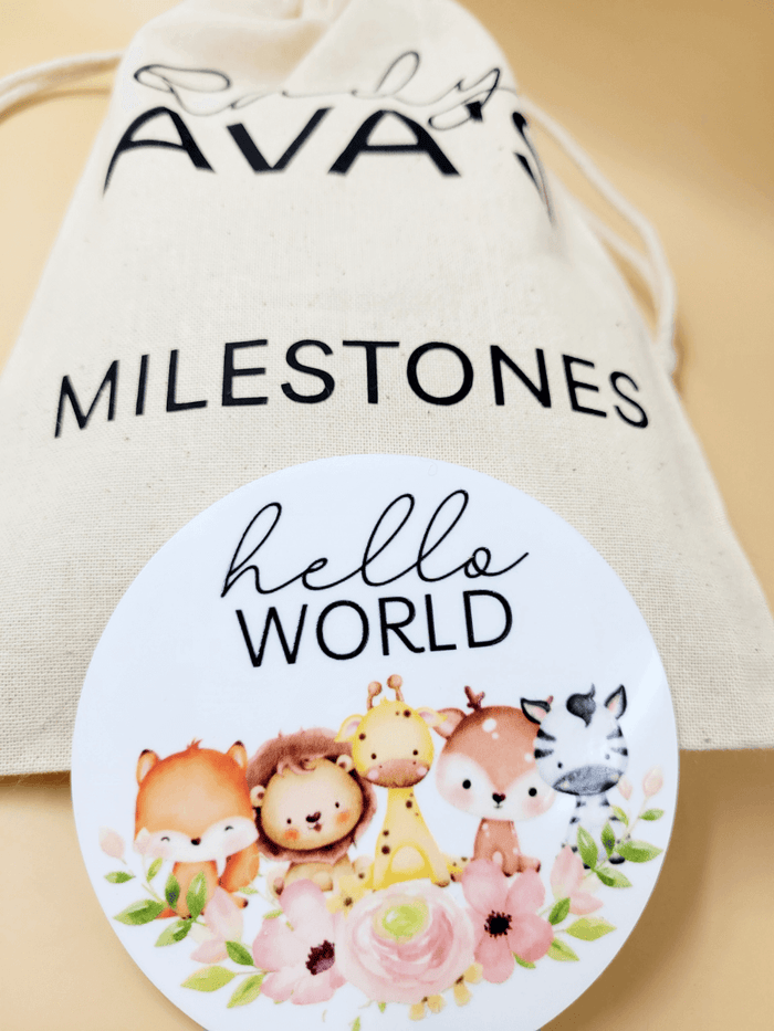 Close-up of personalised baby milestone disc set with a 'Hello World' disc featuring cute animals, packed in a cotton bag.
