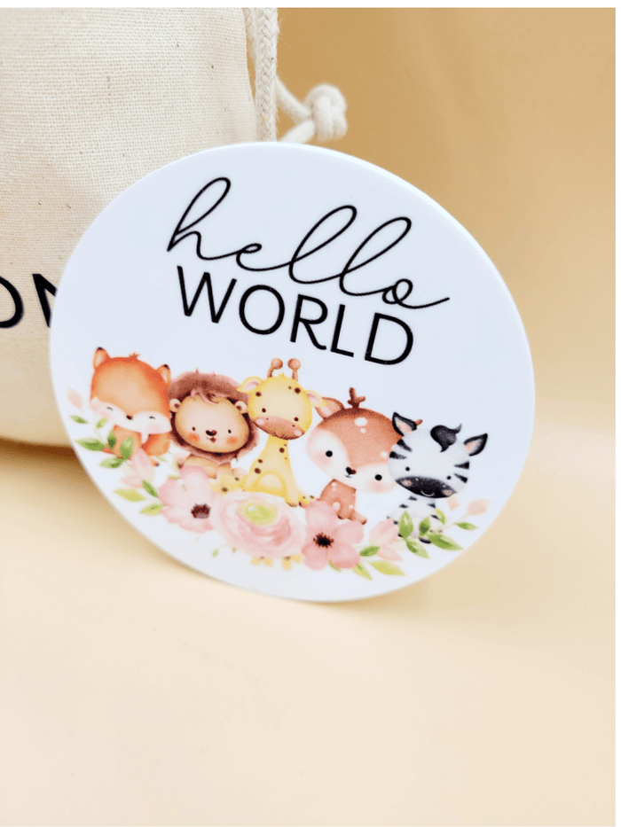 "Hello World" baby milestone disc with animal illustrations on acrylic, part of a personalised milestone set in a cotton bag.