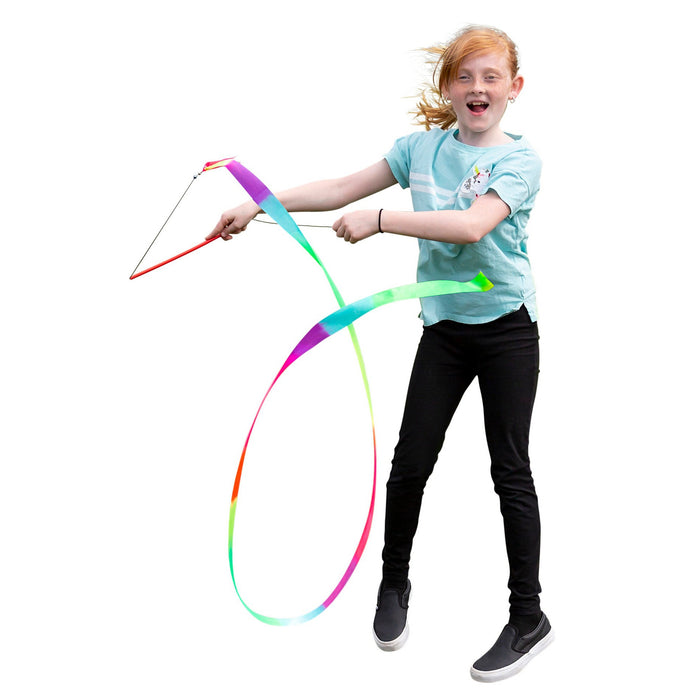 A red-haired girl in a blue t-shirt and black pants smiles as she jumps, holding the Playground Classics Rainbow Stunt Streamer swirling through the air. The white background highlights her energetic, creative movement.