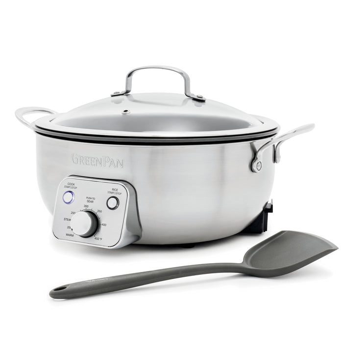 Electric wok with glass lid and control panel next to a gray spatula on a white background.