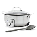 Electric wok with glass lid and control panel next to a gray spatula on a white background.