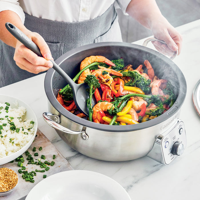 Shrimp stir-fry cooking in a black electric wok, with cooked rice and garnishes on a plate nearby.