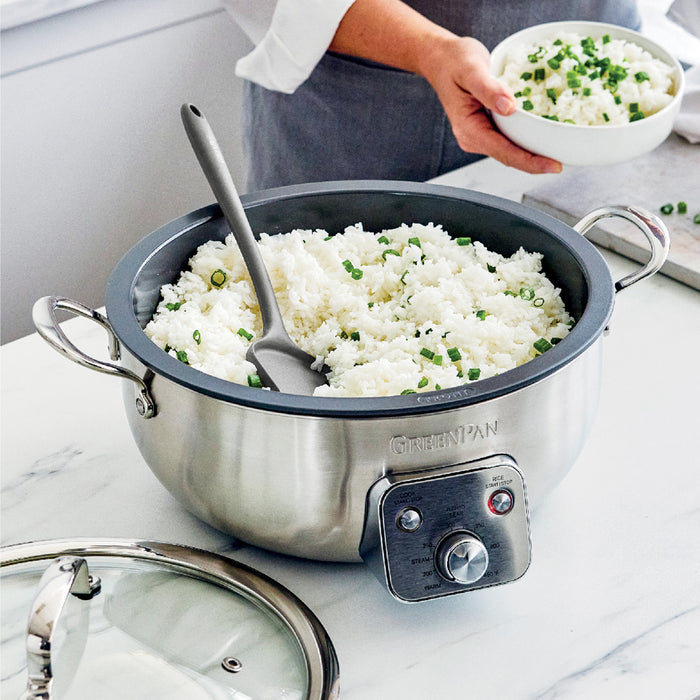 Serving white rice with green onions from a black electric wok on a kitchen counter.