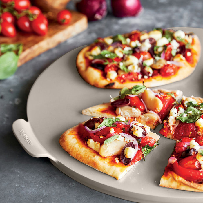 Two vegetable and cheese flatbreads on a gray stone plate next to ceramic nonstick ovenware pieces.