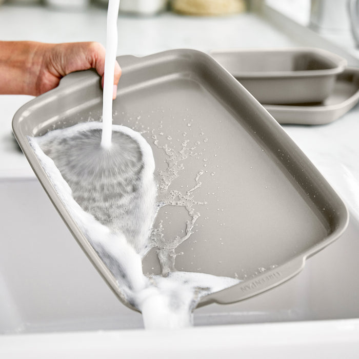 Hand washing a ceramic nonstick 13x9 quarter sheet pan set in a kitchen sink.