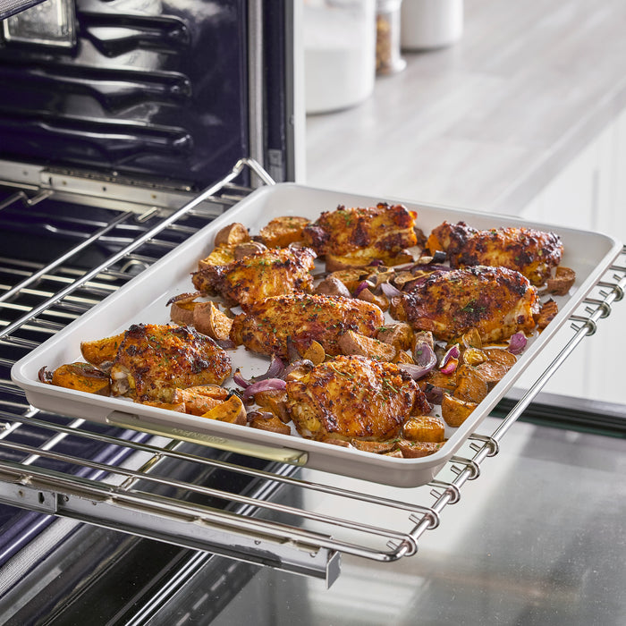 Reserve Bakeware 13″ x 18″ latte-colored half sheet pan holding roasted chicken thighs, potato wedges, and red onion inside an oven.