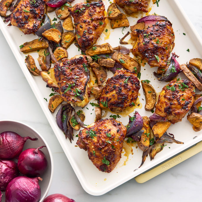 Cream-colored half sheet pan with matching cooling rack, holding roasted chicken, onions, and potatoes.