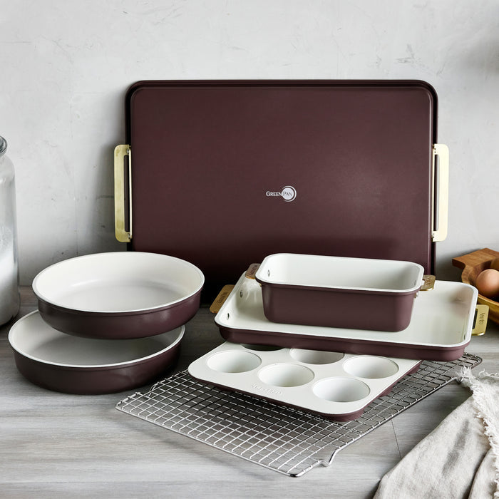 Reserve 7-piece bakeware set in Bordeaux aluminized steel with cream interiors and gold-tone handles.