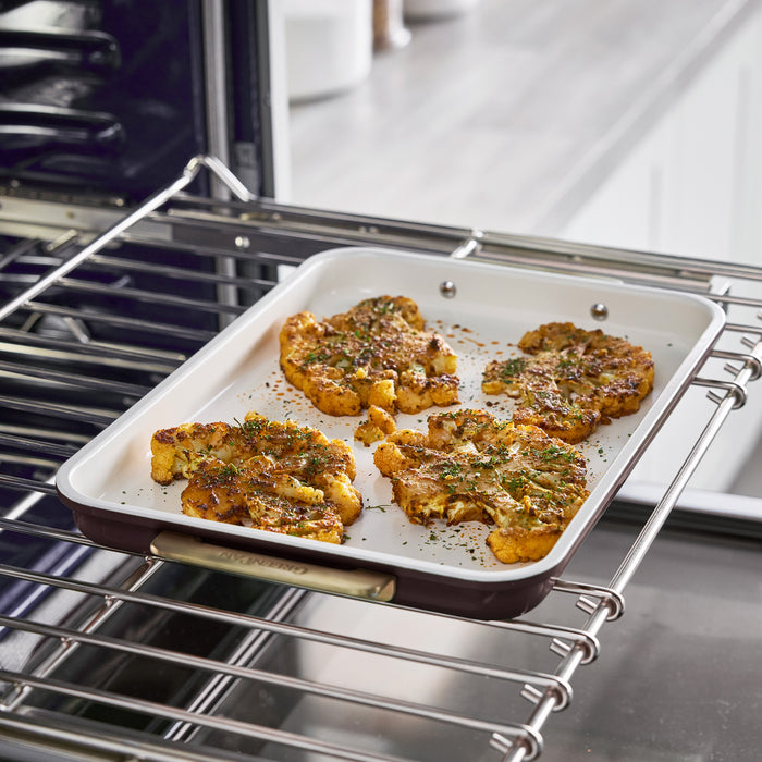 Four roasted cauliflower steaks in a bordeaux Reserve Bakeware 7-piece ceramic baking pan inside an oven.