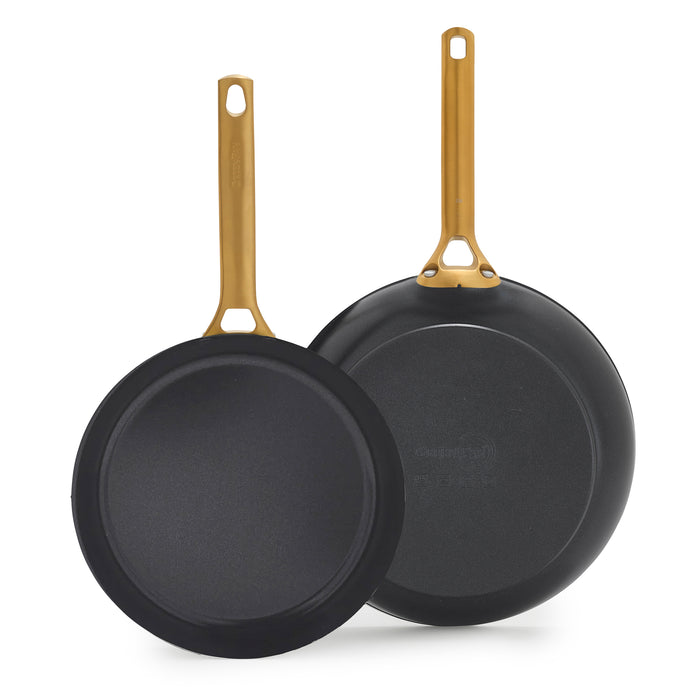 Two black frying pans with gold handles on a white background