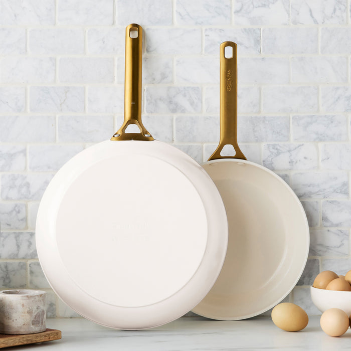 Two cream frying pans with gold handles on a kitchen counter.