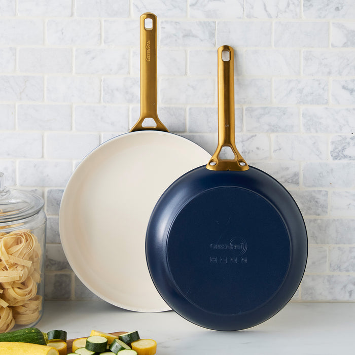 Two dark blue frying pans with gold handles on a kitchen counter.