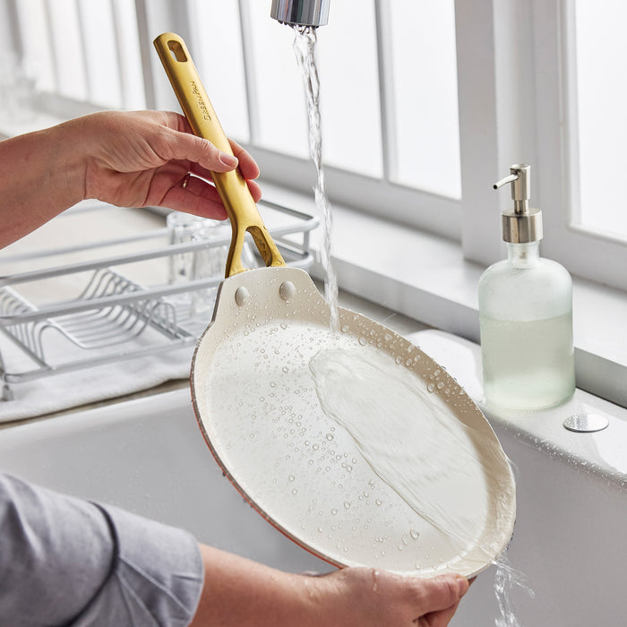 Person washing a crepe pan under running water with soap in a kitchen sink