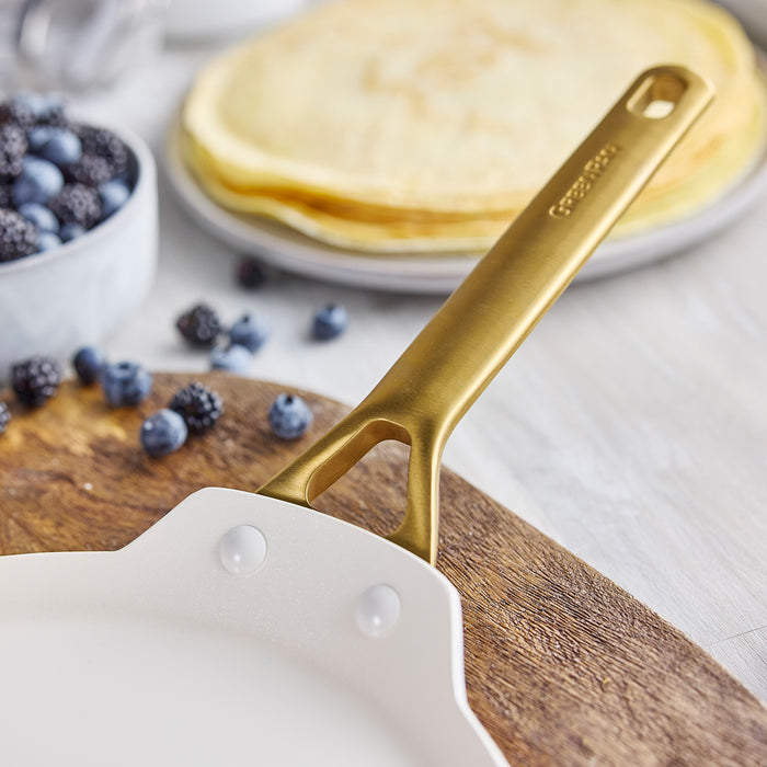 Gold-handled crepe pan with pancakes and berries on a wooden board