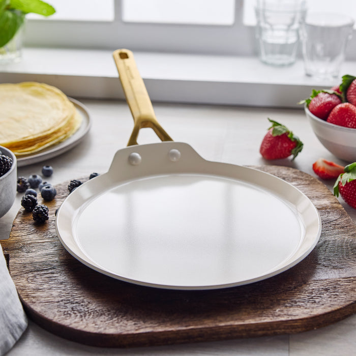 Ceramic nonstick cookware set in twilight blue on a cutting board with berries, crepes, and a window in the background.