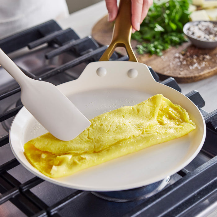 Omelette being folded in a crepe pan with a spatula on a stove.