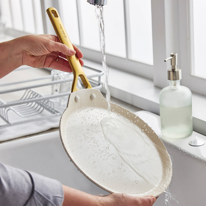 Person washing a crepe pan under running water in a kitchen sink