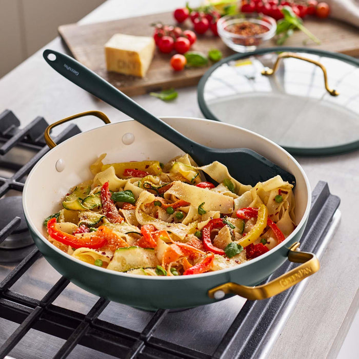 Ceramic nonstick 14-piece cookware set in spruce on stovetop, with a wide skillet of pasta and a spatula nearby.
