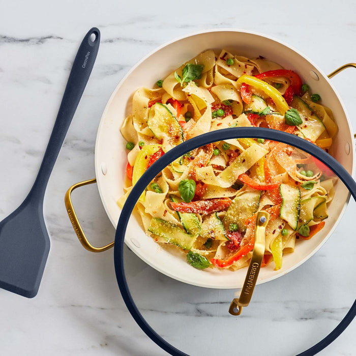 Vegetable ribbon pasta in a twilight blue ceramic nonstick pan with lid on marble, spatula placed beside the pan.