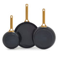 Set of three black frying pans with gold handles on a white background