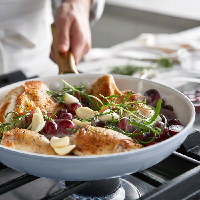 Chicken dish with grapes and herbs in a light blue frypan on a stove.