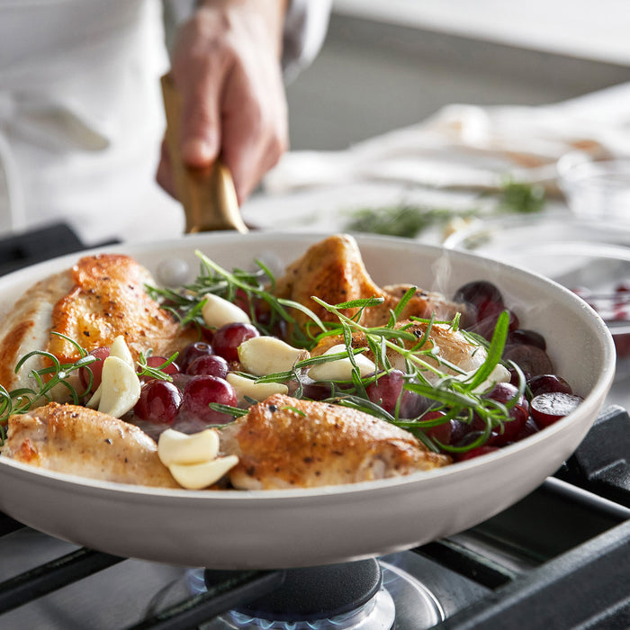 Taupe gray frypan with chicken and grapes and herbs on a stove