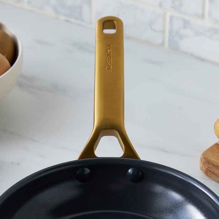 Black frying pan with a gold handle on a marble countertop