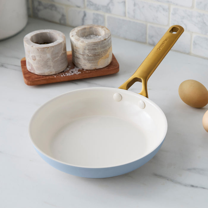 Light blue frying pan with gold handle on a kitchen counter