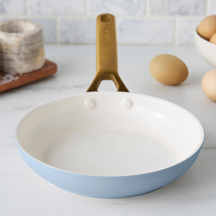Light blue frying pan with a gold handle on a kitchen counter.