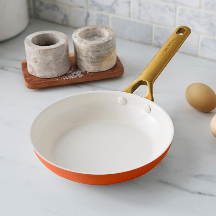 Dark orange frying pan with a gold handle on a kitchen counter.