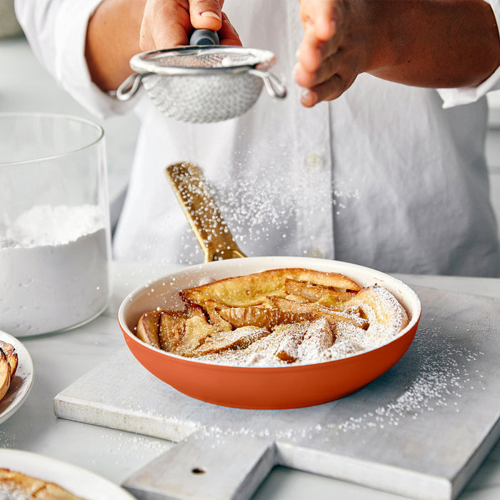 Person dusting powdered sugar over a dish of baked dessert with a strainer.