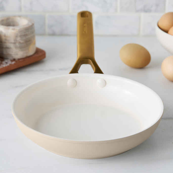Taupe frying pan with a gold handle on a kitchen counter.