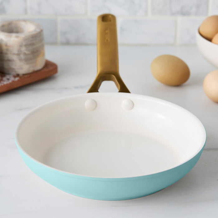 Light blue frying pan with a gold handle on a kitchen counter.