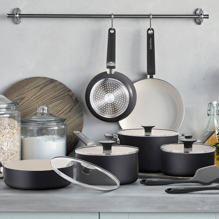 Black 12-piece ceramic nonstick cookware set with glass lids, plus two matching pans hanging on a metal rack above.