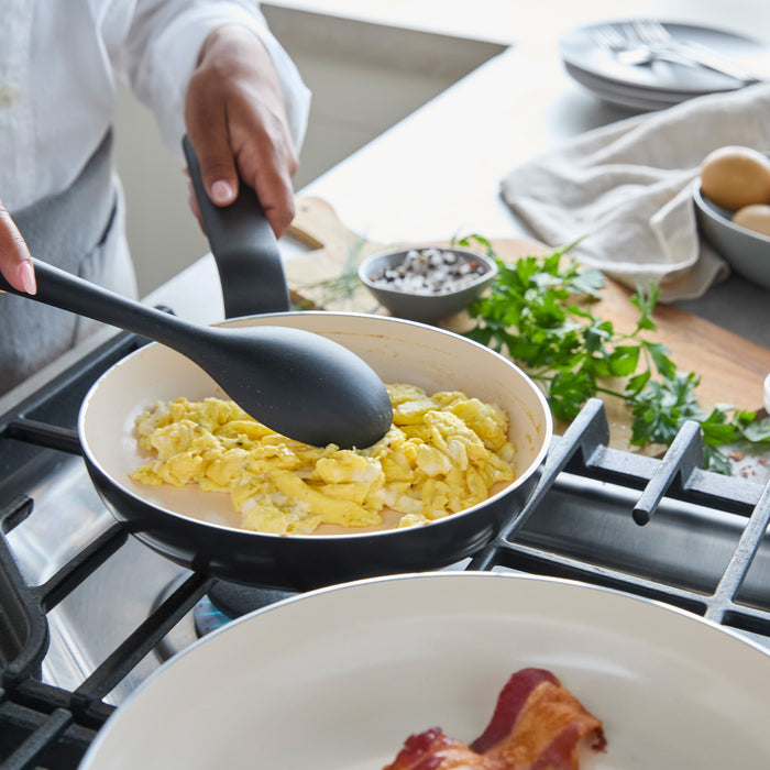 Scrambled eggs in a ceramic nonstick frying pan, with fresh parsley and whole eggs nearby on the countertop.