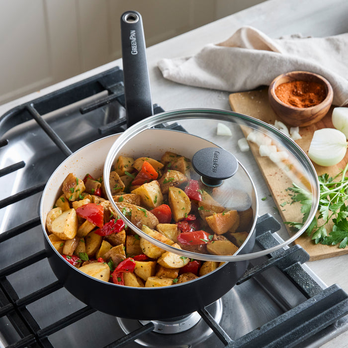 Cooked potatoes and peppers in Rio ceramic nonstick pan on stove, with herbs and spices beside cookware.