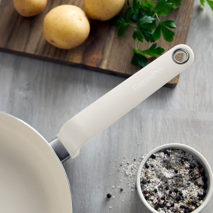 Cream ceramic 12-piece cookware set arranged on wood with potatoes, parsley, salt, and pepper.