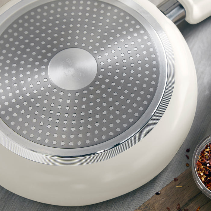 Bottom of a ceramic nonstick frying pan with metal plate and dotted pattern, beside scattered dried spices.
