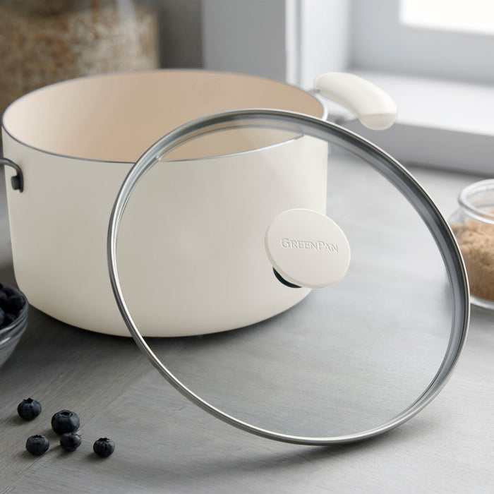 Cream ceramic nonstick 12-piece cookware set with glass lid on counter near blueberries and brown sugar.