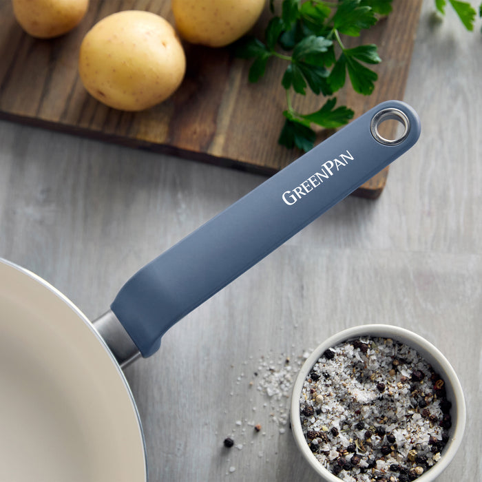 Blue ceramic 12-piece cookware set on a kitchen counter with potatoes, parsley, and salt and pepper shakers nearby.