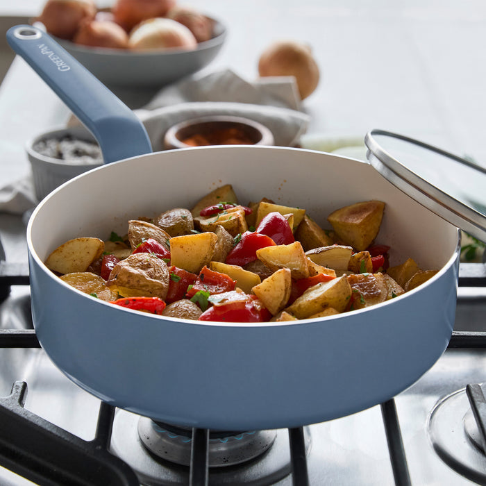 Blue ceramic 12-piece cookware set arranged on a stovetop with roasted potatoes, peppers, and onions beside it.