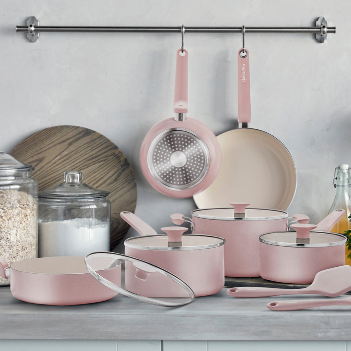 Pink ceramic cookware set with pots, pans, and glass lids arranged on a kitchen counter, 12 pieces total.